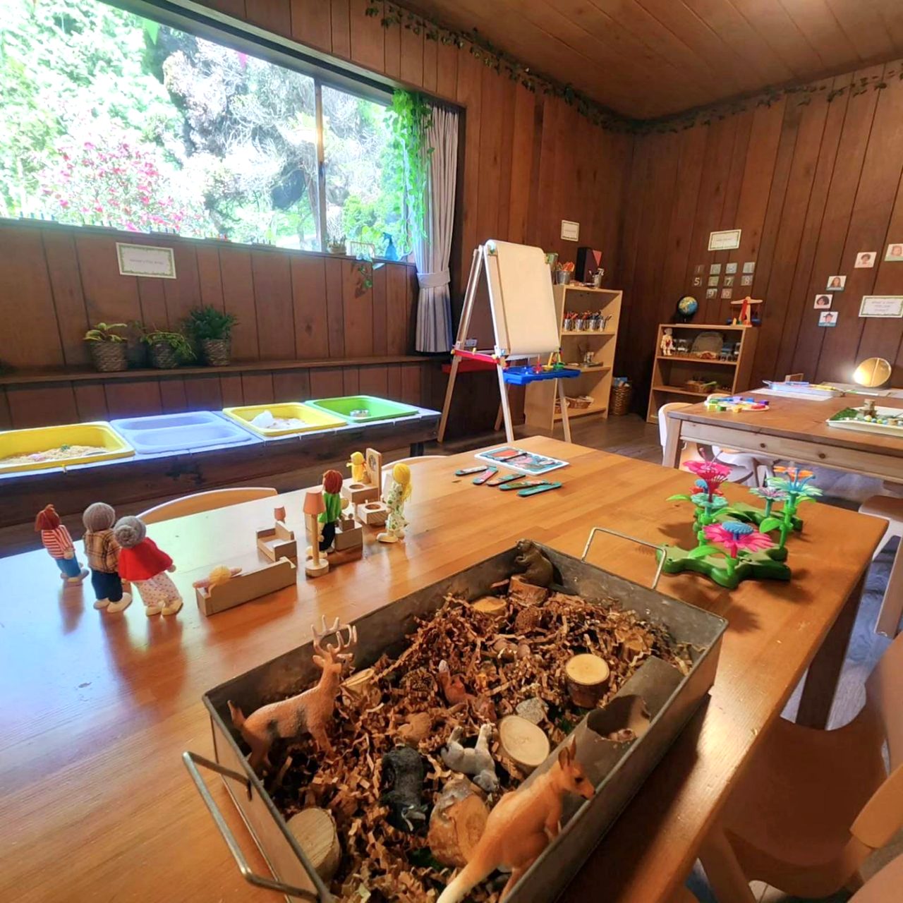 A low table set with small wooden figures, animal play and a nature tray by the window